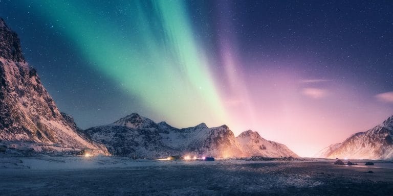 Auroras boreales verdes y púrpuras iluminando el cielo sobre montañas nevadas