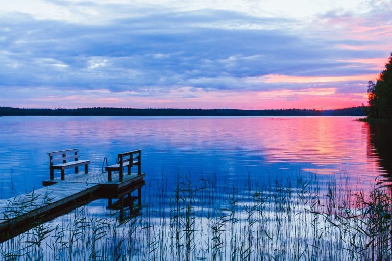 Muelle de madera con bancos frente a un lago en Finlandia durante el atardecer