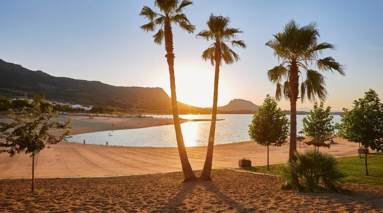 Atardecer en la playa de Peloche en el embalse de García de Sola en Badajoz con palmeras y montañas al fondo
