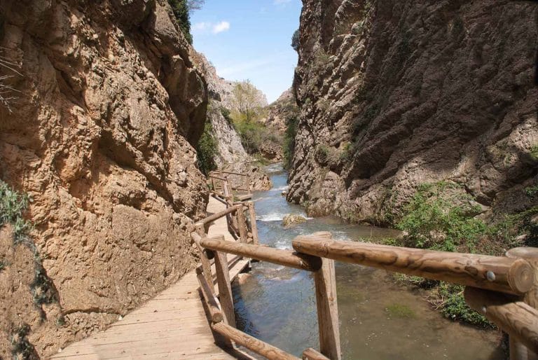 Descenso de agua con barandilla entre montañas en Teruel, rodeado de un paisaje natural impresionante
