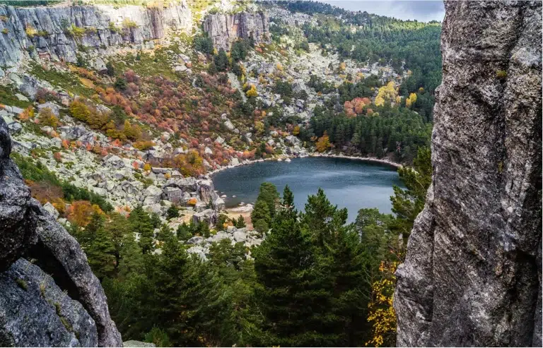 Vista panorámica de la Laguna Negra de Urbión en Soria, rodeada de montañas y vegetación, con colores otoñales.