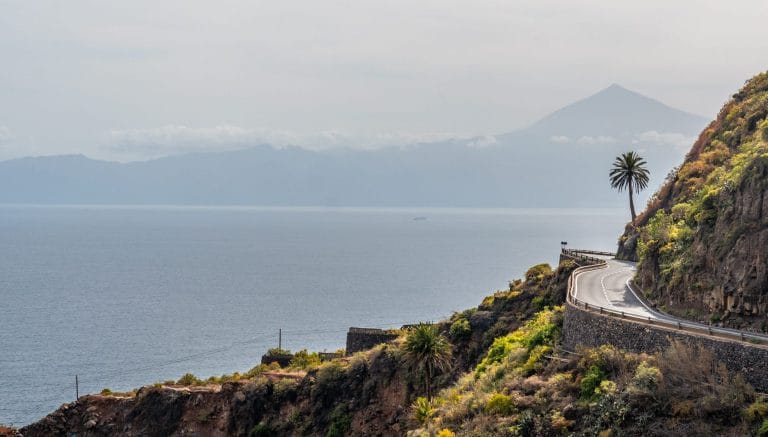 Carretera costera en el pueblo de Agulo, en el norte de La Gomera, con una palmera y Tenerife al fondo