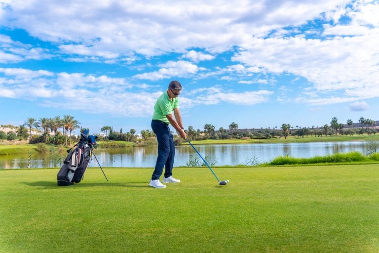Jugador de golf golpeando la bola con driver en un campo profesional junto a un lago