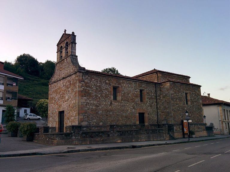 Iglesia de San Julián en Bimenes, Asturias, construida en piedra, con espadaña y rodeada de edificaciones urbanas
