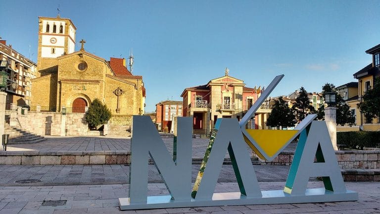 Letras de Nava en la plaza principal del municipio asturiano con iglesia, casas y edificio del ayuntamiento al fondo