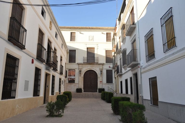 Fachada de la Casa de las Aguas en Montilla con puerta de madera tallada, balcones de hierro y ventanas con rejas bajo un cielo azul.