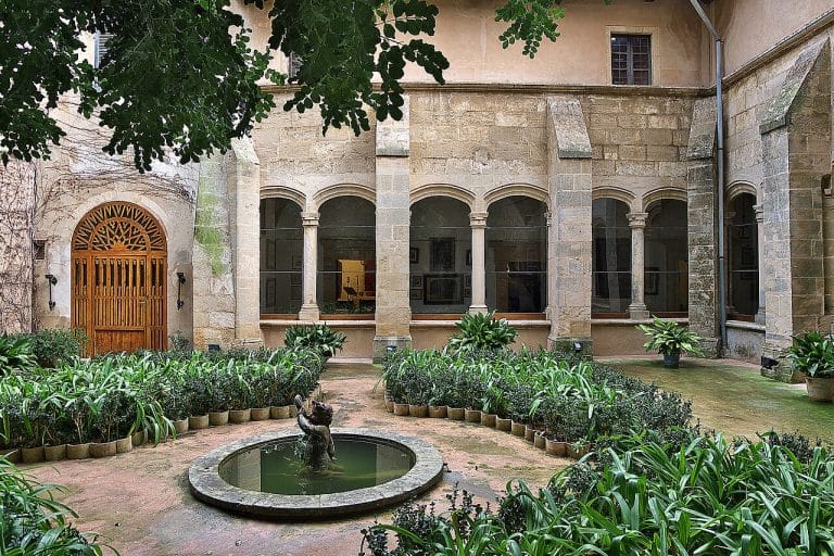 claustro con arcos de piedra, fuente central y abundante vegetación en el palacio del rey sancho en palma de mallorca.