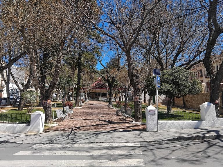 Entrada al Parque Príncipe de España en Doña Mencía con árboles sin hojas, bancos de metal y pasarela de ladrillo bajo un cielo despejado.