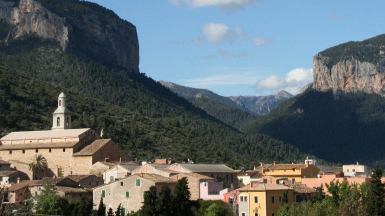 Vista panorámica de Alaró en Mallorca con el Castell d’Alaró en la cima de la montaña y el valle repleto de casas blancas al amanecer.