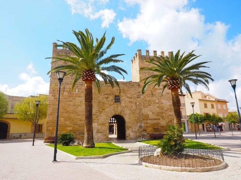 Panorámica urbana de Alcúdia al atardecer con el cielo en tonos cálidos y las luces de la ciudad encendidas bajo el horizonte