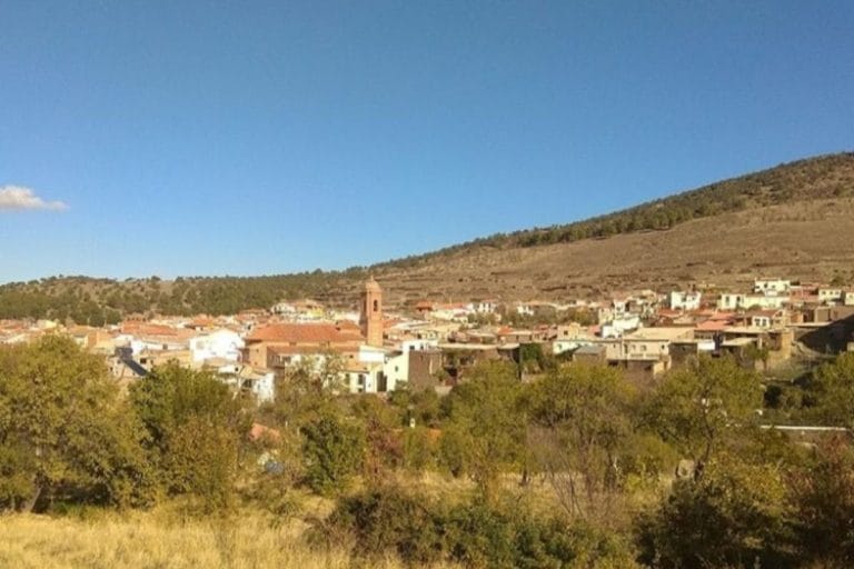 Pueblo de Granada con casas de tejados rojizos y un campanario en la falda de una colina bajo un cielo azul.