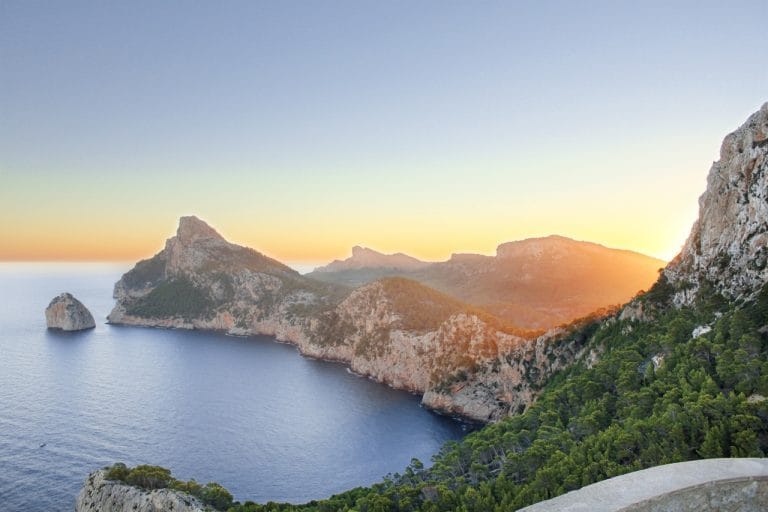 Amanecer en Cap de Formentor en Mallorca con acantilados rocosos, montañas al fondo y luz dorada sobre el mar Mediterráneo