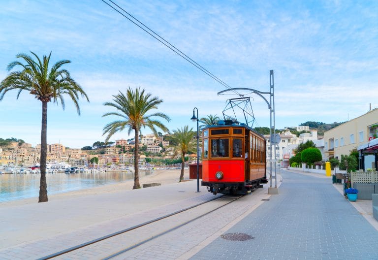 Antiguo tranvía junto a la playa de Port Soller en Mallorca en verano, flanqueado por palmeras.