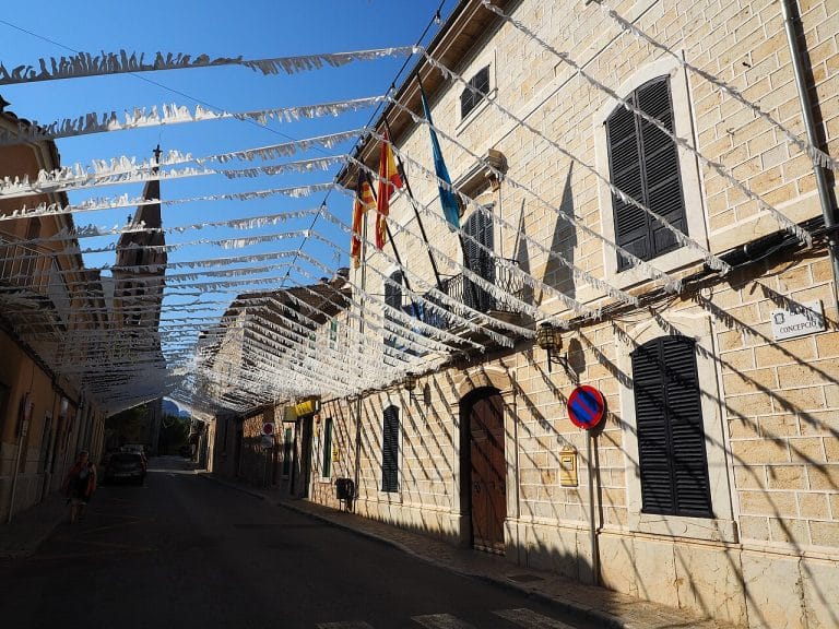 calle adoquinada decorada con guirnaldas blancas y fachadas de piedra con contraventanas negras en Binissalem, Mallorca.