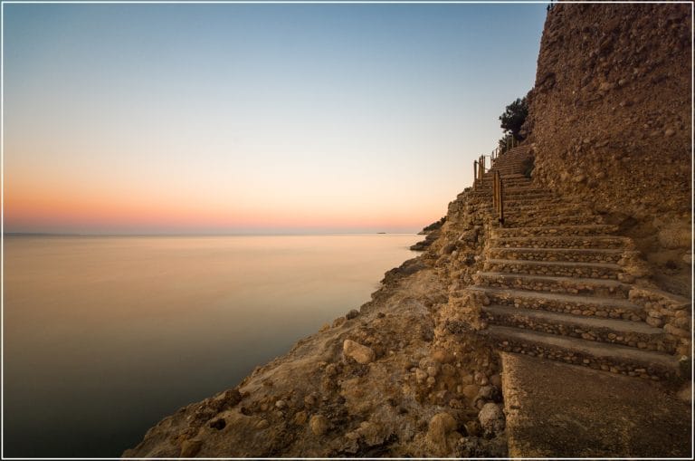 escaleras talladas en el acantilado junto al mar tranquilo al atardecer en cala vinyes, españa.