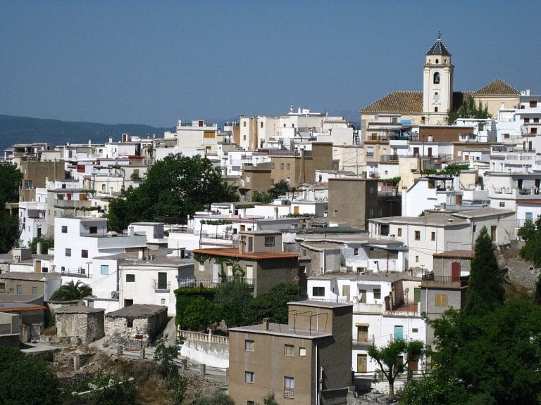 vista panorámica de un pueblo de casas blancas apiladas en la ladera, con un campanario destacándose bajo un cielo despejado.