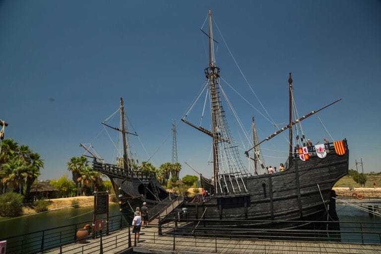 Réplicas de las carabelas de Cristóbal Colón atracadas junto a un muelle de madera con visitantes subiendo por una pasarela.