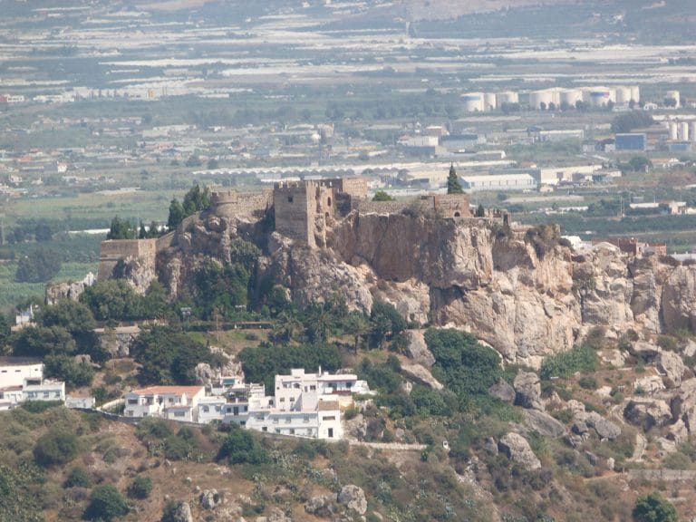 Castillo de Salobreña sobre un promontorio rocoso con casas blancas al pie y campos agrícolas al fondo bajo un cielo despejado.