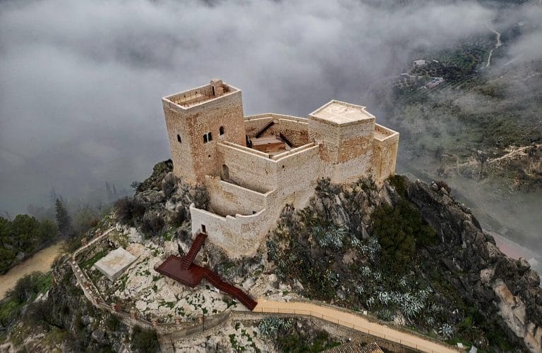 Castillo de Luque tras su restauración en 2024 visto desde el aire con muros de mampostería y nubes bajas sobre el valle.