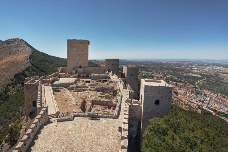 Panorámica del castillo de Santa Catalina en Jaén con sus murallas y torreones sobre un cerro, con el valle de olivares al fondo.