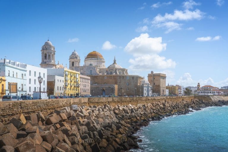 Vista de la catedral de Cádiz junto al paseo del Vendaval con el malecón y el mar en primer plano.