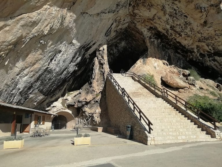 Escalera de piedra con barandales conduce a la entrada de la cueva de Artá, excavada en una gran formación rocosa.