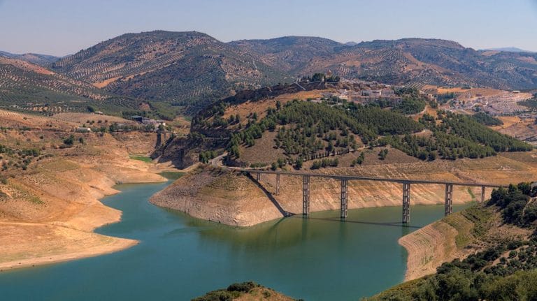 Vista panorámica del embalse de Iznájar en Andalucía, con un puente elevado y rodeado de montañas y pinares