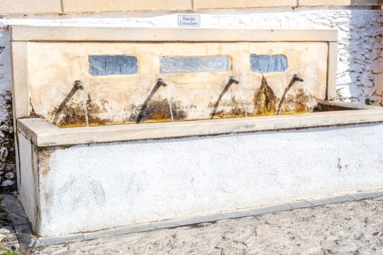 antigua fuente lavadero de piedra con cuatro caños de agua fluyendo contra un muro encalado y un gran pila rectangular para lavar ropa, en el pueblo de bubión.