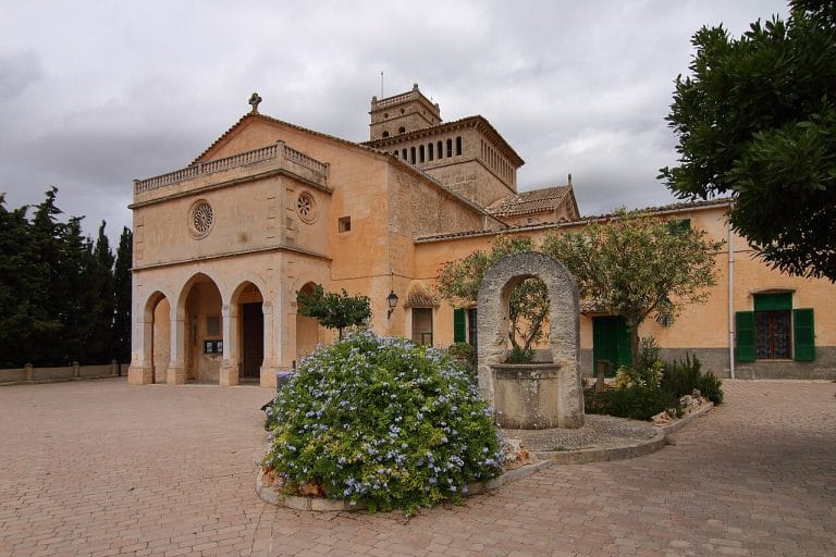 Fachada de la Iglesia de Nuestra Señora de Atocha en Ariany, Mallorca, con torre campanario y muro de piedra bajo un cielo despejado