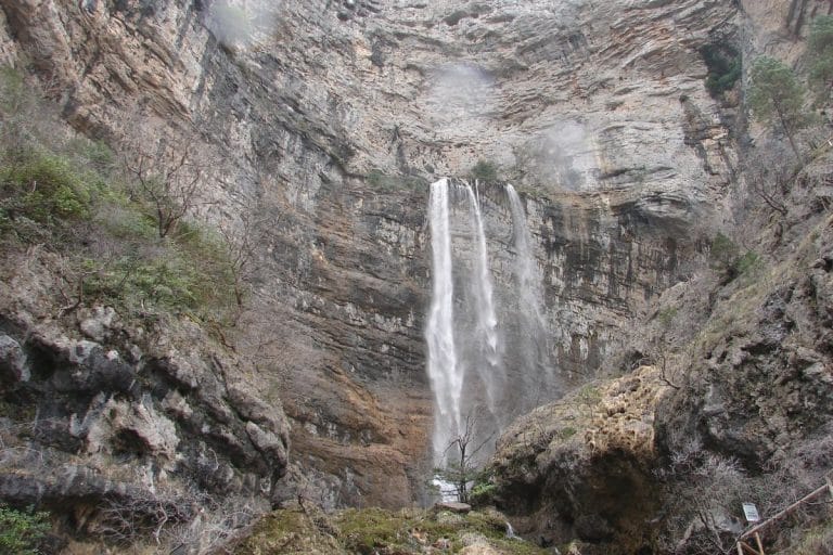 Nacimiento del río Mundo con cascadas que caen por una pared rocosa y agua fluyendo sobre piedras musgosas en primer plano.
