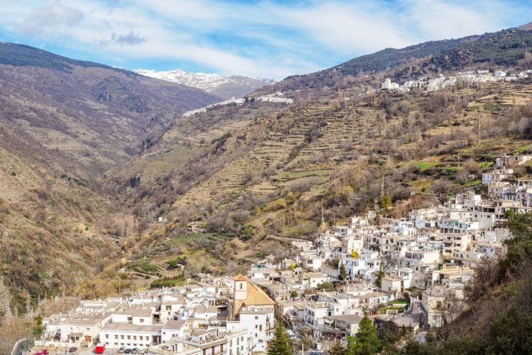 panorámica de los pueblos blancos de pampaneira, búbion y capileira en la ladera de la sierra con bancales y cumbres nevadas a lo lejos.