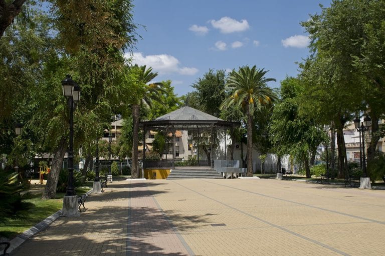 Paseo de Rojas en Lucena con quiosco de música rodeado de palmeras y bancos en un parque urbano.