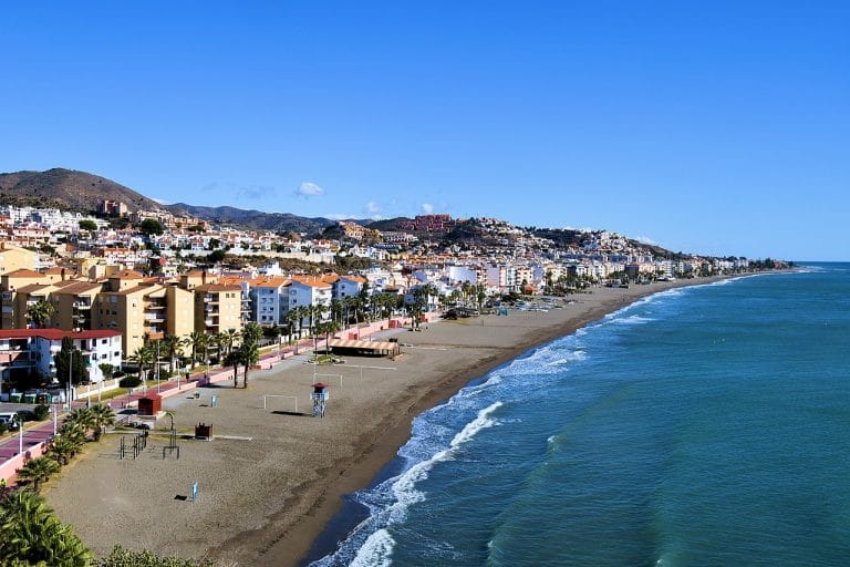 Vista panorámica de la playa y el paseo marítimo en Rincón de la Victoria, Málaga, con edificios y colinas al fondo