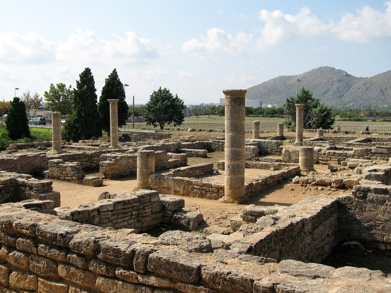 Ruinas de Pollentia en Mallorca con muros antiguos y restos arqueológicos rodeados de pinos.