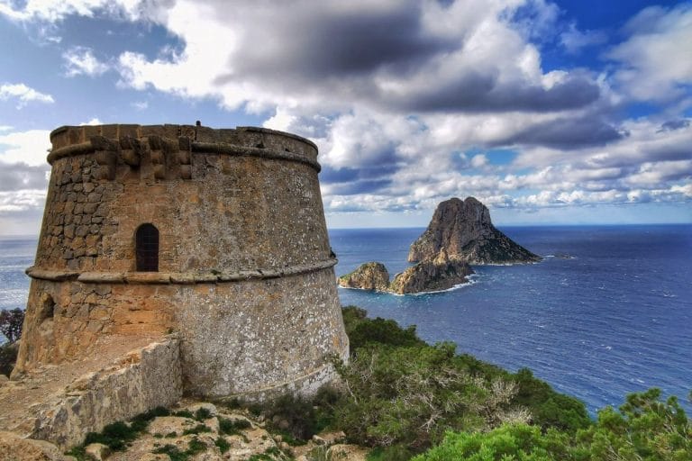 La torre des Savinar en primer plano con la isla de Es Vedrá al fondo y el mar.