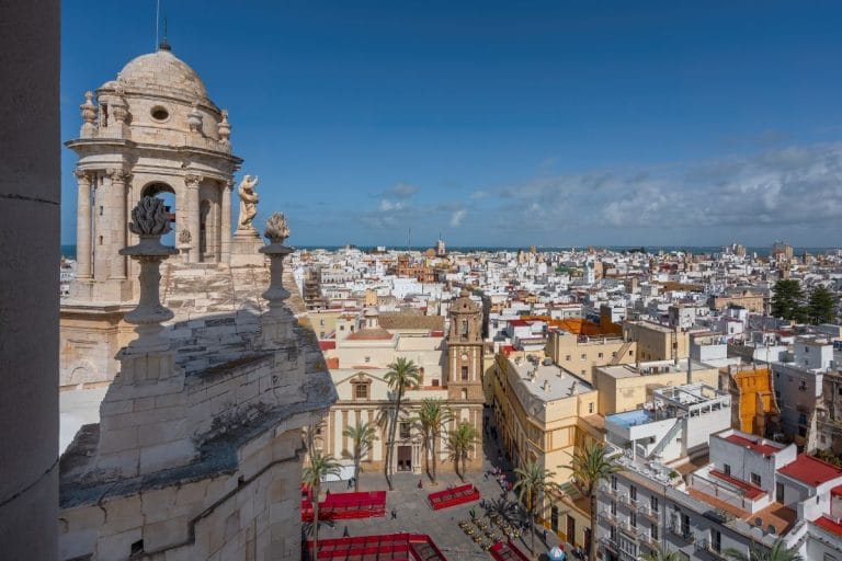 Vista aérea de la plaza de la Catedral de Cádiz con la torre y cúpula de la catedral y las casas blancas de la ciudad hasta el mar al fondo.