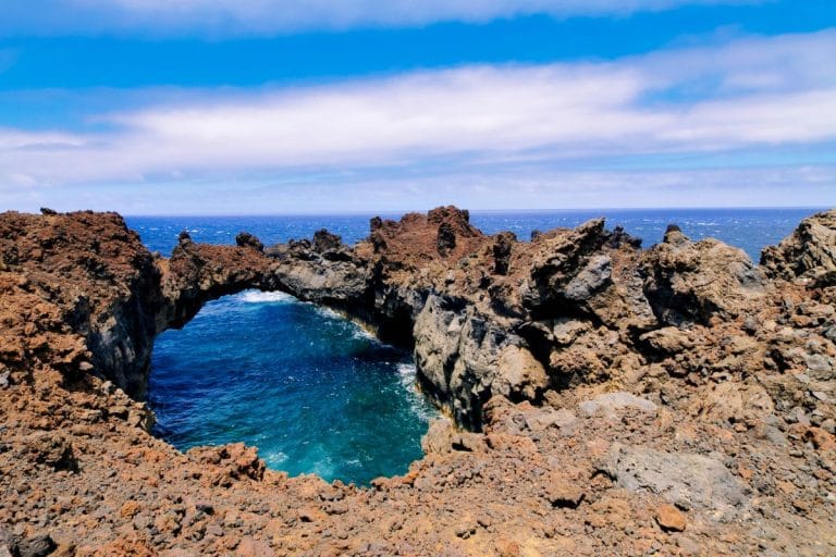 Formación rocosa del Arco de la Tosca en El Hierro, con el mar azul intenso al fondo y lava erosionada formando un puente natural.