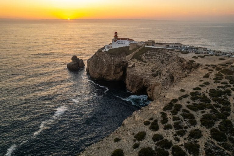 Vista desde las alturas de la playa de Beliche en Sagres al atardecer, con acantilados y surfistas en el mar.