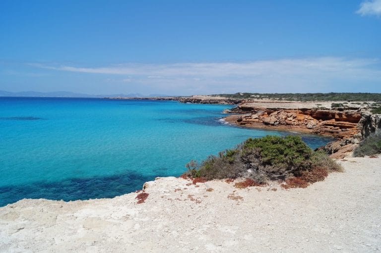 Vista de Cala Saona en Formentera con agua turquesa, rocas y playa bajo un cielo azul despejado