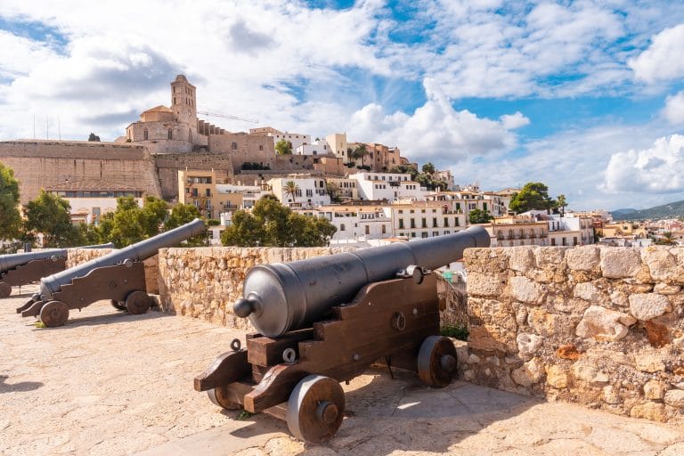 Cañones medievales en la muralla del castillo de Ibiza con la ciudad blanca y el cielo azul al fondo