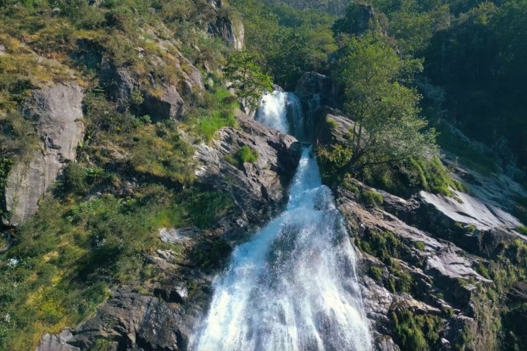 Cascada de Belelle en Fene, Galicia, con el agua descendiendo entre rocas y vegetación en un paisaje natural