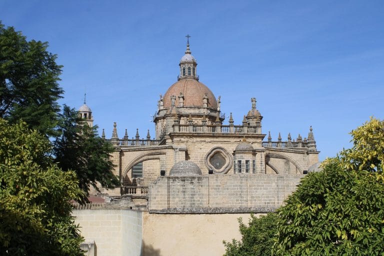 Vista frontal de la Catedral de Jerez de la Frontera con su cúpula y detalles góticos, ambas flanqueadas por naranjos en primer plano.