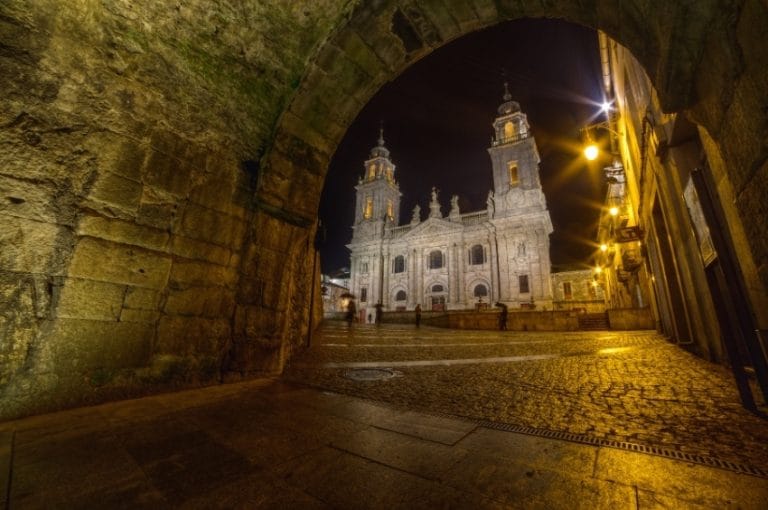 Vista nocturna de la Catedral de Santa María de Lugo, Galicia, iluminada, vista a través de un arco de piedra