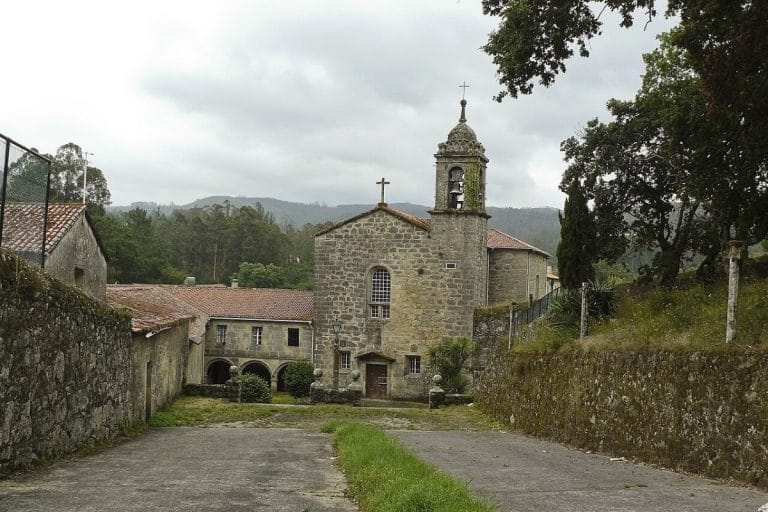 Fachada del convento franciscano de Herbón, rodeado de vegetación y montañas, en un entorno rural de Galicia.
