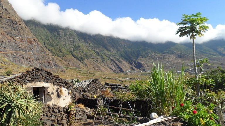 Casas tradicionales de piedra volcánica en el Ecomuseo de Guinea, con el paisaje montañoso y nubes rasantes de El Hierro al fondo.