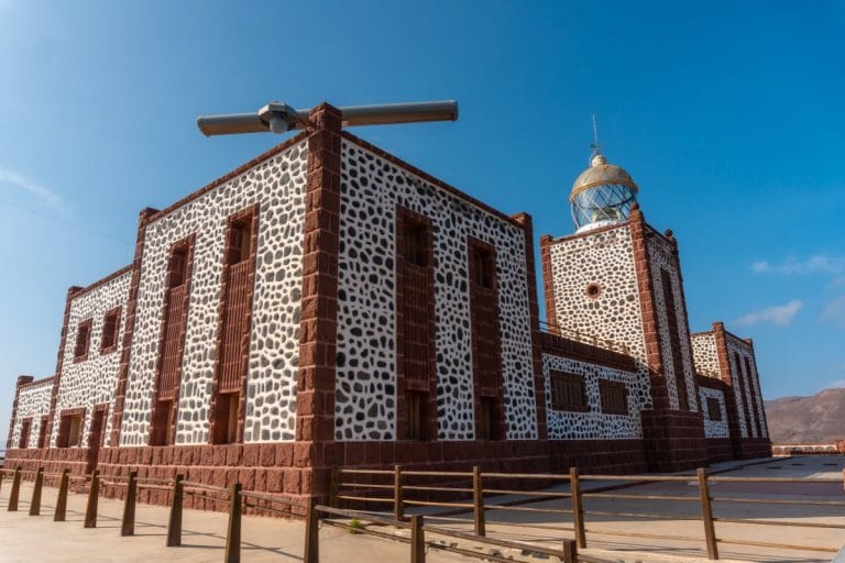 Vista panorámica del Faro de La Entallada en Las Playitas, Fuerteventura, un emblemático edificio junto al acantilado con arquitectura tradicional canaria y cielo despejado.