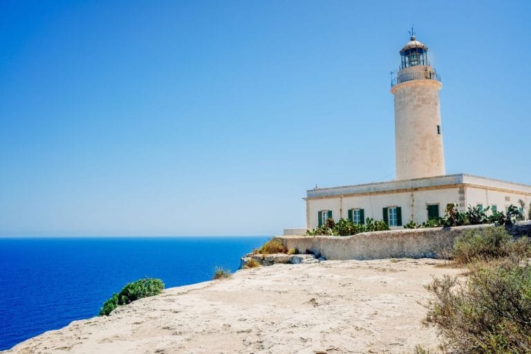 Faro de La Mola situado sobre un acantilado con mar azul y cielo despejado al fondo