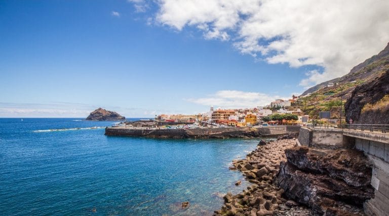 Vista panorámica del pueblo costero de Garachico en Tenerife, con casas coloridas junto al mar, costa volcánica y el islote característico al fondo.
