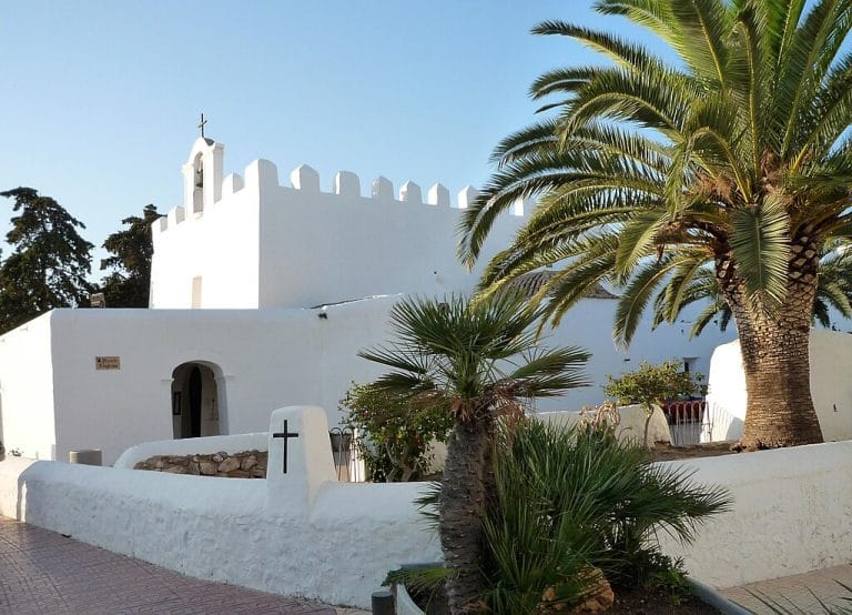 Fachada de la iglesia blanca de Sant Jordi en Ibiza con palmeras y cielo despejado