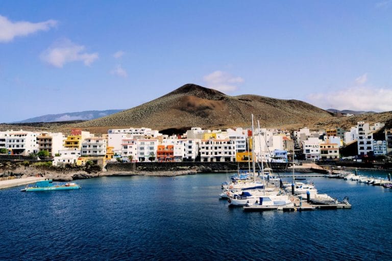 Vista del puerto de La Restinga en El Hierro, con edificios de colores frente al mar y un paisaje volcánico al fondo.